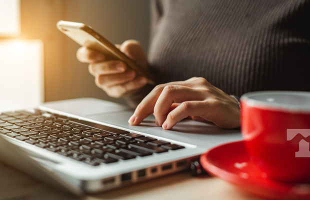 Consumer at a laptop computer with a mobile phone in hand.