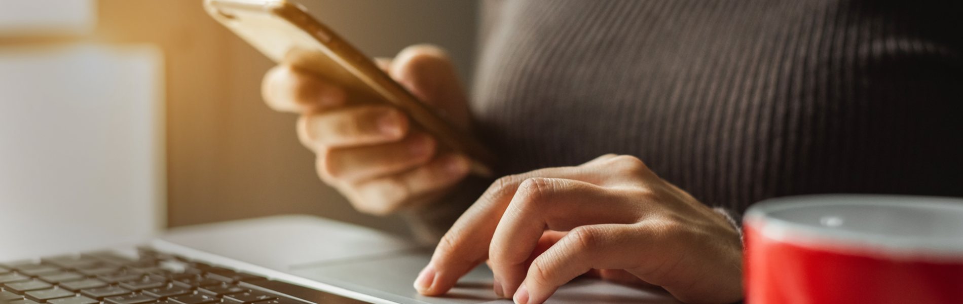 Consumer at a laptop computer with a mobile phone in hand.